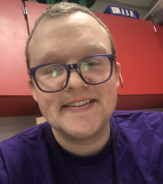 Joshua Malek in a purple t-shirt and glasses